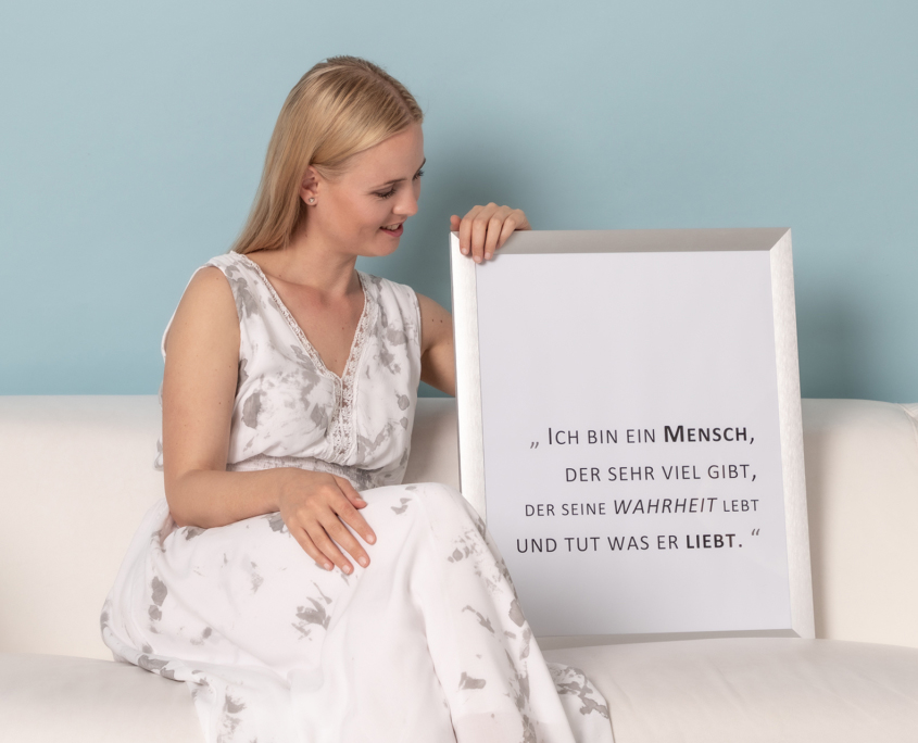 Bianca Rammer sitzend auf einer Couch. Neben ihr ein Bilderrahmen mit einem individuellem Gedicht.